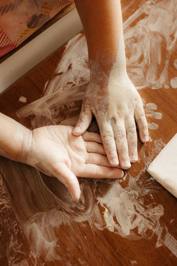 Child hands painting with white paint on a wooden table